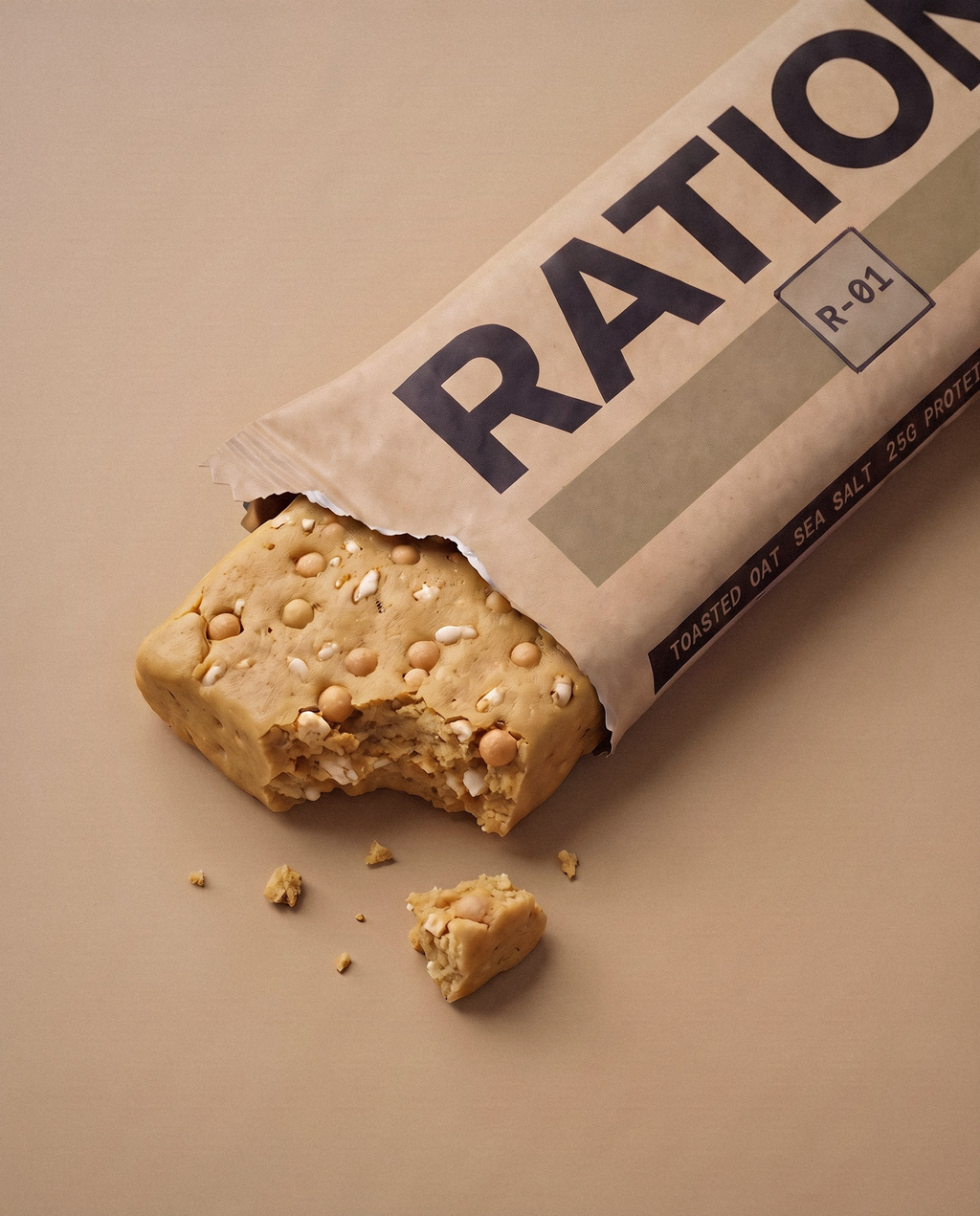 Studio render of the R-01 Toasted Oat · Sea Salt bar peeking out of its torn-open printed wrapper: the flavor band color across the matte-paper pack, imperfect hand-pressed edges and a few crumbs on a neutral studio background.